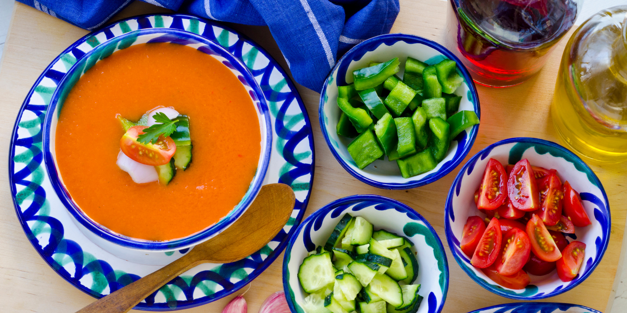 bowl of gazpacho with small bowls of green bell pepper, cucumber, tomato on the side
