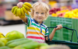 child in grocery store holding up bananas
