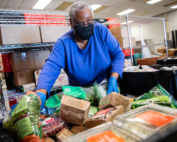 A volunteer in a blue shirt sorts a pile of packaged food