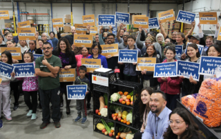 Advocates holding signs that say "Food 4 all" in ACCFB's warehouse