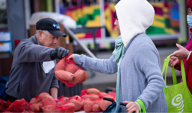 A food bank volunteer handing a bag of produce to a shopper at an outdoor market (placeholder — replace per instance)